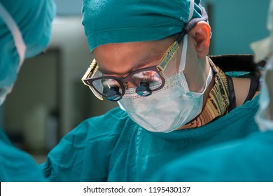 Surgeon Performs Vascular Surgery In Operating Theater Using  Surgical Loupe To Magnify Blood Vessel.