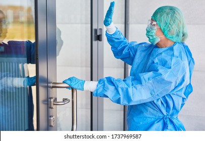 Surgeon In Protective Clothing In Front Of Clinic Makes Hand Signals At The Door To The Entrance To The Covid-19 Pandemic