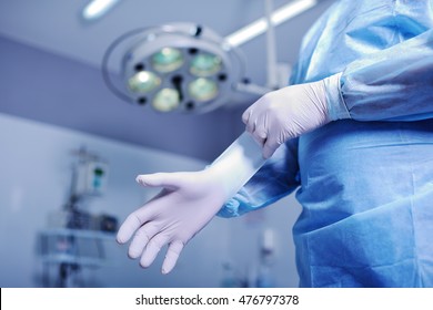 Surgeon putting on sterile rubber gloves to complicated surgical operation on the background lights. Surgery