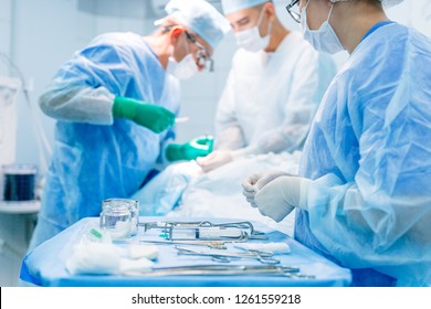 Surgeon working with a scalpel, wearing a blue surgical mask and a surgical cap in intensive care with his team of surgeons
