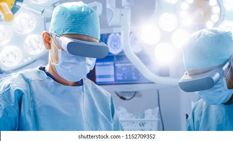 Surgeons In Augmented Reality Glasses Perform State Of The Art Surgery In High Tech Hospital. Doctors And Assistants Working In Operating Room.