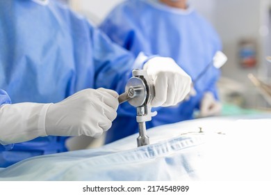 Surgeons Hands Close Up Performing Surgery. Surgeon Using Drill Machine During Procedure. Doctors Are Wearing Protective Workwear In Operating Room.