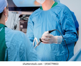 The surgeon's hands in latex gloves and blue uniforms hold special medical instruments during laparoscopic surgery. Treatment of proctological diseases.
