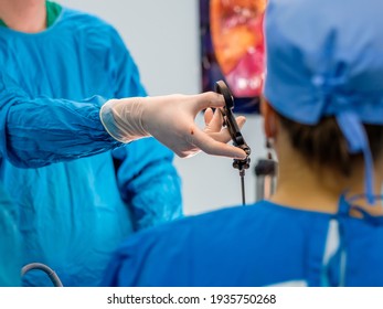 The surgeon's hands in latex gloves and blue uniforms hold special medical instruments during laparoscopic surgery. Treatment of proctological diseases.