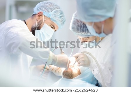 Surgeons and nurse during a dental operation.Anesthetized patient in the operating room.Installation of dental implants or tooth extraction in the clinic. General anesthesia during orthodontic surgery