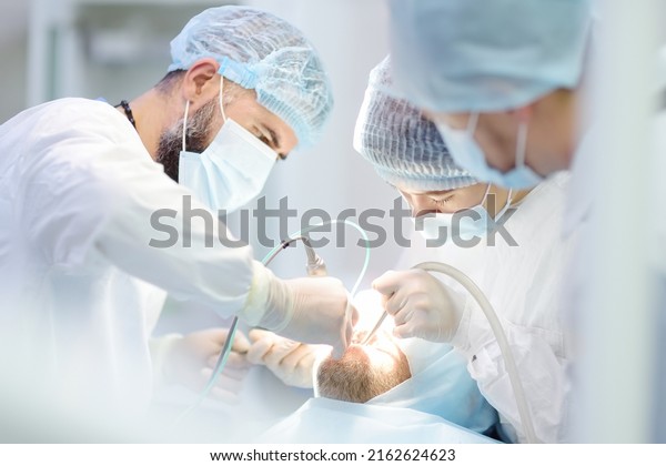 Surgeons and nurse during a dental\
operation.Anesthetized patient in the operating room.Installation\
of dental implants or tooth extraction in the clinic. General\
anesthesia during orthodontic\
surgery