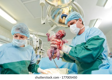 Surgeons Perfoming Surgery Operation Of Abdominal Cesarean Section During Child Delivery Birth At Clinic Operating Room