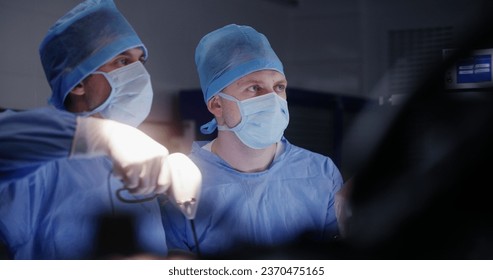 Surgeons perform laparoscopy and look at monitors in operation room. Nurse talks with doctors and checks condition of patient during difficult surgery. Medical staff at work in clinic or hospital. - Powered by Shutterstock