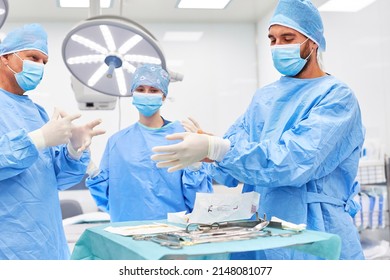 Surgeons In Protective Clothing And With Face Masks Put On Disposable Gloves Before The Operation