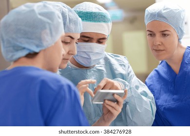 surgery, medicine and people concept - group of surgeons with smartphone in operating room at hospital - Powered by Shutterstock