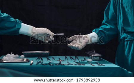 Surgery team operating in a surgical room.Assistant passing surgical scalpel to the doctor. Hand of doctor in white glove. Two surgeons working and passing surgical equipment in the operating room