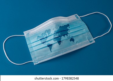 Surgical Face Mask With A Map Of The World On Blue Background. COVID-19 Pandemic Concept.