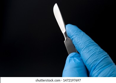 Surgical Instruments In Operating Room And Doctor Performing Surgery Concept Theme With A Surgeon Hand Wearing Blue Latex Gloves And Holding A Scalpel Isolated On Black Background With Copy Space