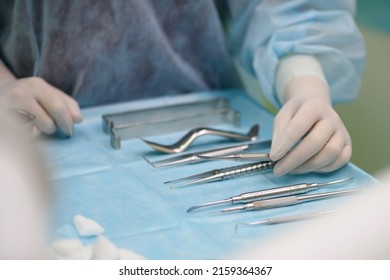 Surgical instruments in the operating room. A nurse in a surgical suit and gloves is preparing for a tooth implant operation.
				Dental probe, tweezers, scalpel, needle holder, rasps on instrument table.