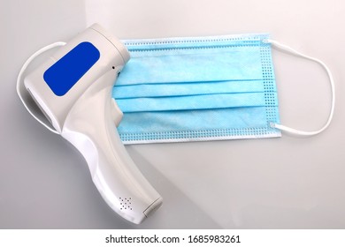 A Surgical Mask And An Infrared Forehead Thermometer Isolated On White.