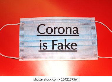 Surgical Mask In A Red Background With The Sign Corona Is Fake, Concept Of Covid Fake News