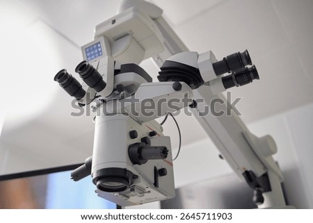 Surgical microscope positioned in modern operating room, advanced optical equipment featuring multiple eyepieces and adjustment controls used for precision medical procedures