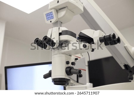 Surgical microscope positioned in modern operating room, advanced optical device featuring multiple eyepieces and adjustable arms used for precision medical procedures