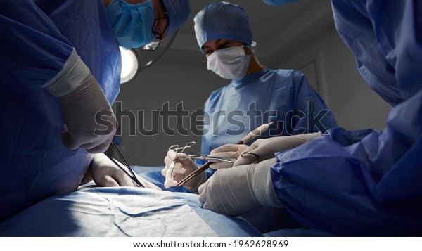 Surgical team in blue medical suits using\
medical instruments and performing surgical operation. Focus on\
surgeon hands doing cosmetic surgery at hostpital. Concept of\
medicine and plastic\
surgery.
