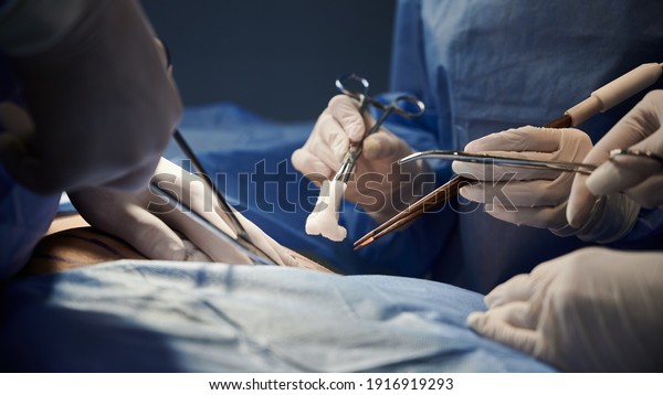 Surgical team in blue suits using medical\
instruments and performing surgical operation. Close up surgeon and\
assistants doing cosmetic surgery in modern clinic. Concept of\
medicine, plastic\
surgery.