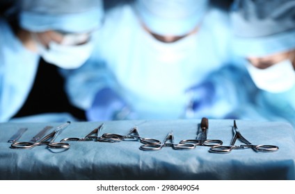 Surgical tools lying on table wile group of surgeons at background operating patient in surgical theatre. Steel medical instruments ready to be used. Surgery and emergency concept