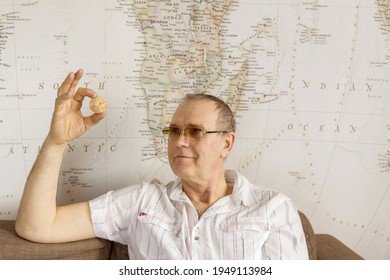 Surgut, Russia - March 27, 2021: A Portrait Of  A 65 Year Old Smiling Man With Wooden Puzzle In The Hand On Light Background. Dementia Therapy With Wooden Puzzle. 