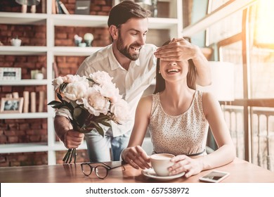 Surprise! Beautiful romantic couple in cafe. Young man is presenting flowers to his beloved. Feel of happiness. - Shutterstock ID 657538972