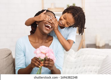 Surprise Concept. Laughing african woman holding flowers, little girl covering her eyes, copyspace