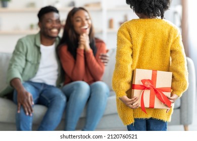 Surprise Gift. Little Girl Hiding Present For Her Mommy Behind Her Back, Small Daughter Surprising African American Mom At Home, Greeting Happy Excited Woman With Mother's Day, Selective Focus