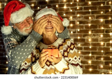 Surprise for her. Christmas event and celebration, Senior couple with Santa hats exchange a present - Shutterstock ID 2231400069