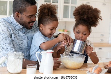 Surprise for mommy. Attentive smiling african daddy or adult elder brother showing small daughter and son or younger kids siblings how to prepare dough for tasty pancakes on healthy lunch at kitchen - Powered by Shutterstock