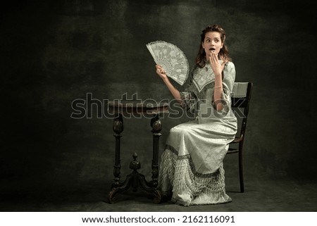 Surprise. shock. Vintage portrait of young beautiful girl in gray dress of medieval fashion style isolated on dark background. Comparison of eras concept, flemish style. Classic art character, old