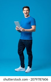 Surprise young handsome Caucasian man smiling and holding laptop computer in isolated light blue studio background