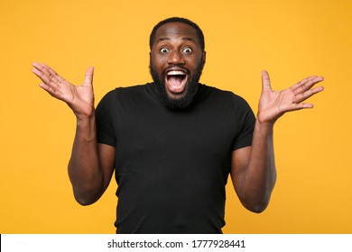 Surprised african american man guy football fan in casual black t-shirt isolated on yellow background studio portrait. People lifestyle concept. Mock up copy space. Keeping mouth open spreading hands