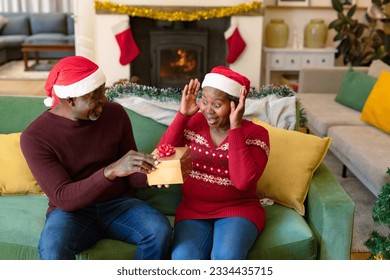 Surprised african american senior couple in santa hats sharing presents at christmas time. retirement lifestyle and christmas festivities, celebrating at home. - Powered by Shutterstock