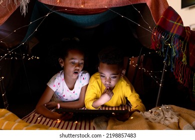 Surprised african american siblings lying in makeshift tent, using tablet. childhood, christmas, festivity and tradition at home. - Powered by Shutterstock