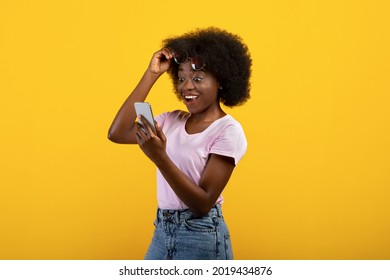 Surprised african american woman looking at smartphone in excitement, lifting her sunglasses over yellow studio background. Emotional black lady learning about online summertime sale - Powered by Shutterstock