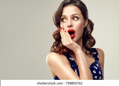 Surprised and amazed girl holds  her cheeks and looks aside .  Beautiful woman with curly hair and red nails. Expressive facial expressions.