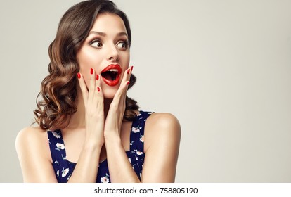Surprised and amazed girl holds  her cheeks and looks in the side .  Beautiful woman with curly hair and red nails. Expressive facial expressions.  Presenting your product. 
