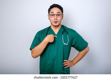 Surprised And Ambushed Asian Male Physician, Nurse In Scrubs Pointing At Himself, Beaing Named Or Chosen, Standing White Background