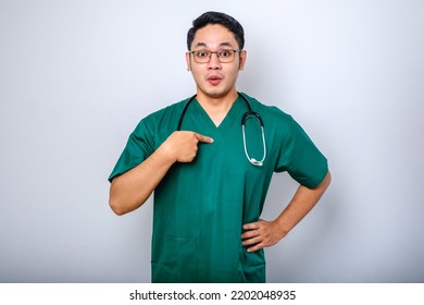 Surprised And Ambushed Asian Male Physician, Nurse In Scrubs Pointing At Himself, Beaing Named Or Chosen, Standing White Background