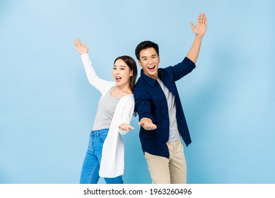 Surprised Asian Couple Standing Back To Back Smiling And Opening Hands In Light Blue Isolated Studio Background