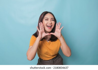Surprised Asian woman reclines on her hands and shouting while looking at the camera over blue background