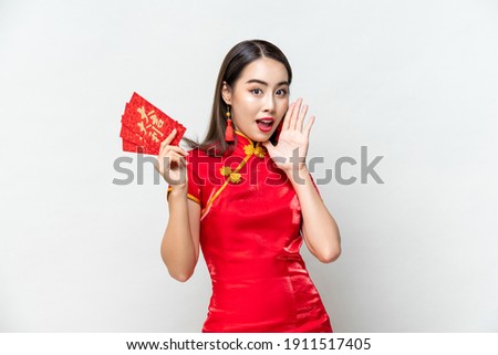 Surprised Asian woman in traditional oriental costume holding red envelopes or Ang Pao in gray isolated background, Chinese text means great luck great profit