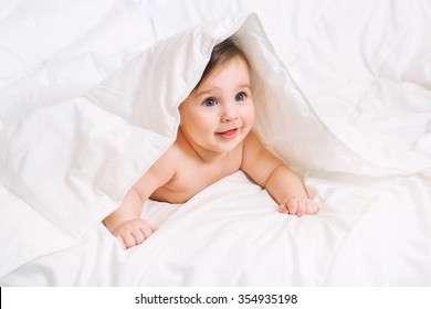 Surprised Baby lies on the bed under the blanket