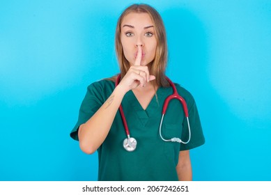 Surprised Beautiful young doctor woman wearing medical uniform over isolated background makes silence gesture, keeps finger over lips and looks mysterious at camera