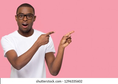 Surprised Black Man Pointing Fingers At Copy Space Looking At Camera, Amazed African American Guy Feeling Astonished Excited Advertising Product Or Service Isolated On Pink Blank Studio Background