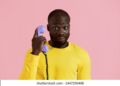 Surprised Black Man Talking On Retro Phone On Pink Background. Colorful Portrait Of Amazed African American Male Model With Shocked Face Expression Calling On Purple Landline Phone