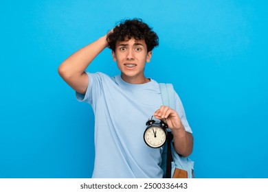 Surprised boy guy high school male pupil student teenager with dental braces backpack holding alarm clock isolated over blue background. Time management education back to school concept - Powered by Shutterstock