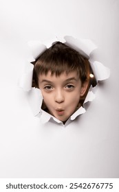 Surprised boy peeks through a torn paper hole, showing excitement and curiosity. Isolated on a white background, perfect for themes of discovery, wonder, and childhood imagination
